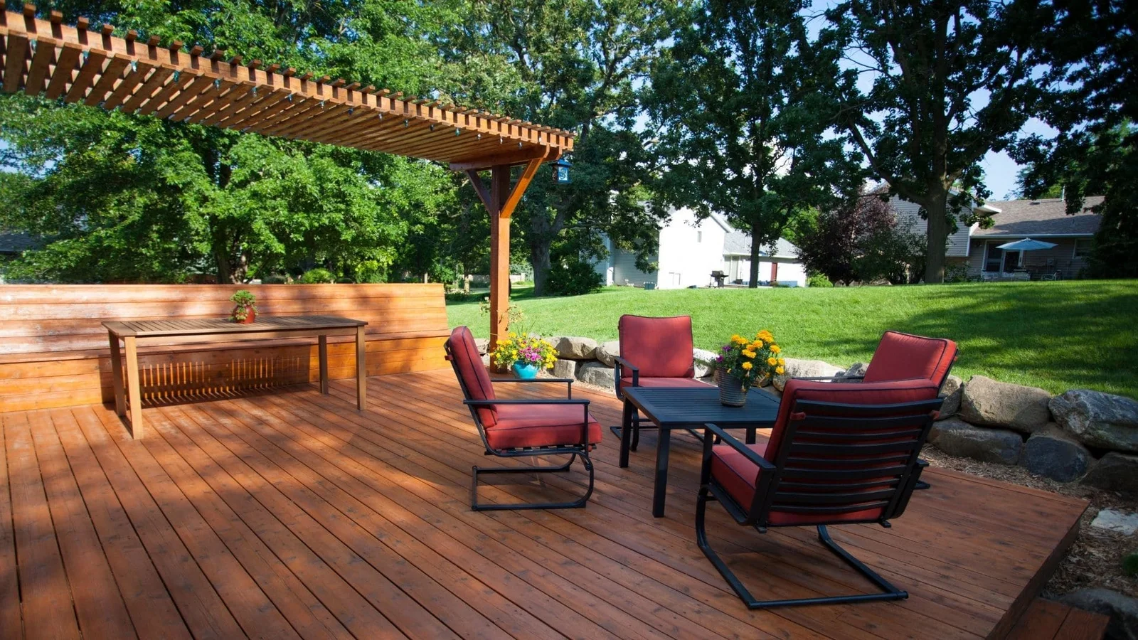 Wooden deck with pergola, built-in bench, and metal patio chairs with burgundy cushions