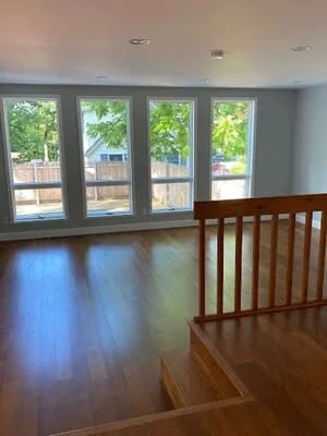 Interior room with four large windows overlooking trimmed trees and landscape, hardwood flooring visible