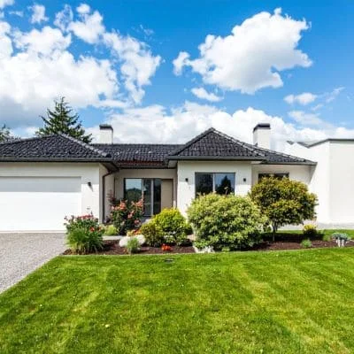 Manicured lawn with pruned shrubs and evergreen trees in front of white modern home