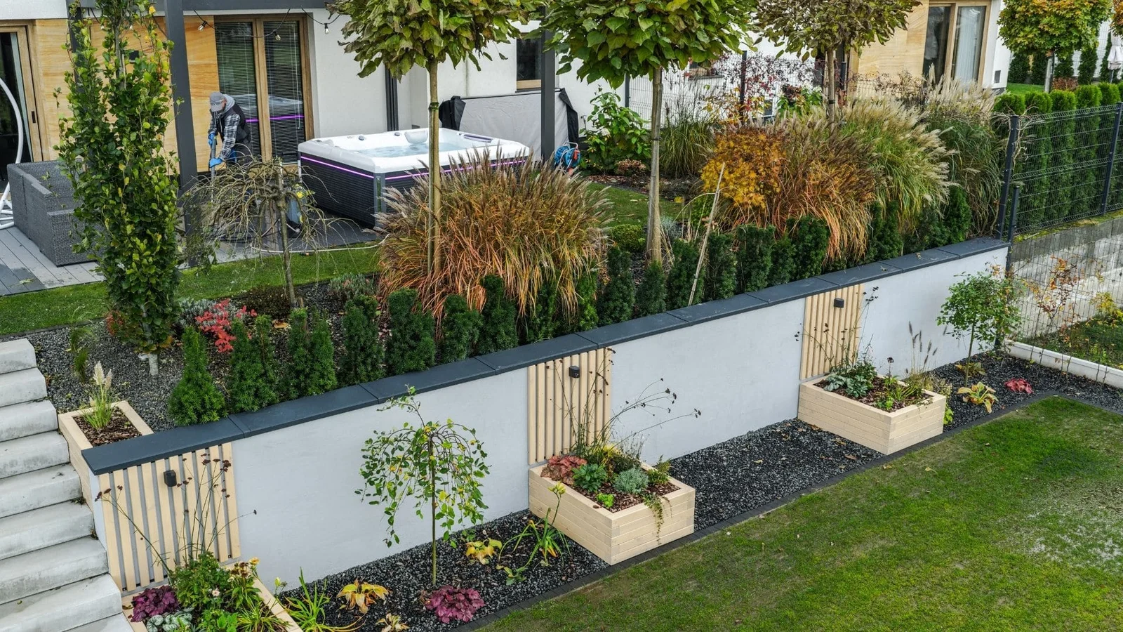 Raised wood planting beds with black coping, ornamental grasses, evergreens, and stone mulch in modern backyard