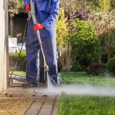 Worker in blue uniform pressure washing brick pavers with red-handled equipment