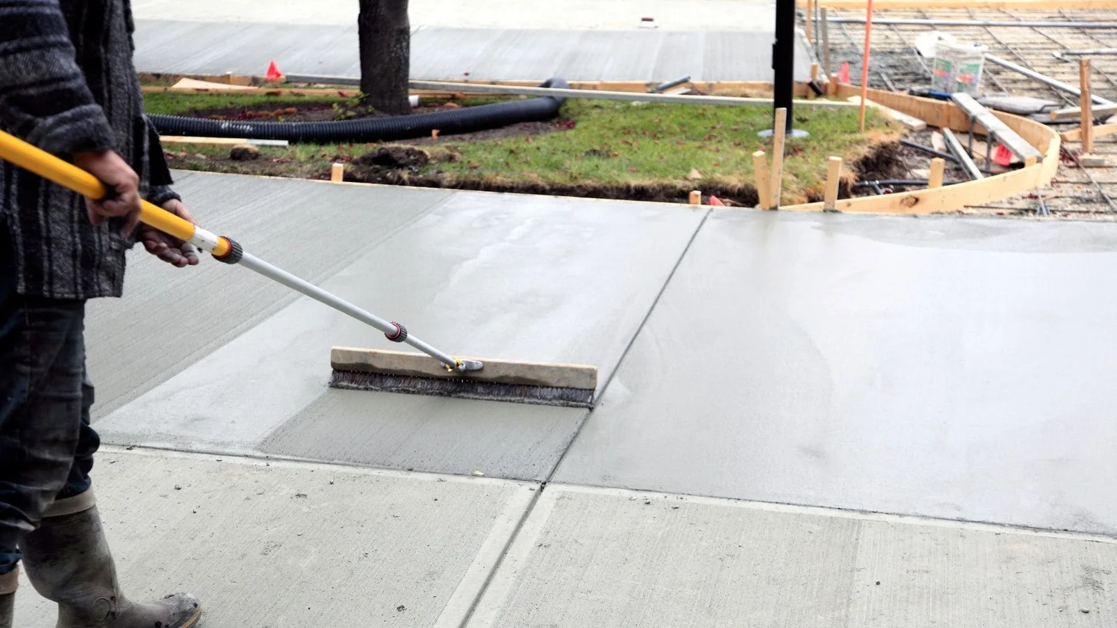Worker applying brush finish to concrete slab with sealing compound using long-handled tool