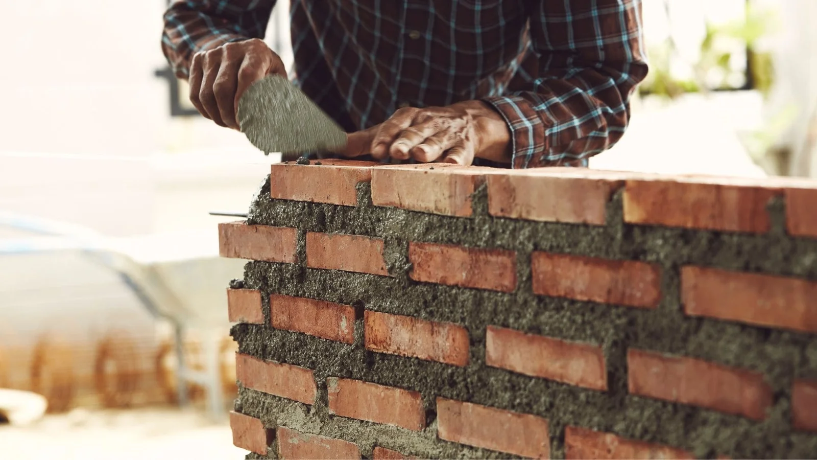 Mason applying mortar between clay bricks in running bond pattern during construction